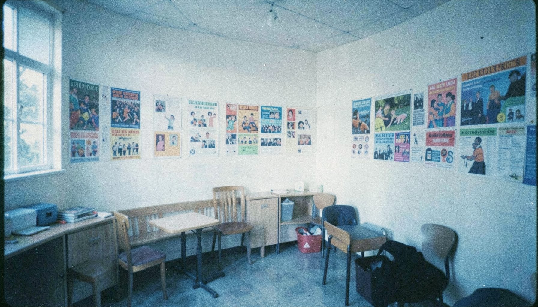 Photographie argentique aux tons bleus apaisants et blancs, grain subtil, montrant une salle commune lumineuse avec des affiches colorées, évoquant l'entraide et la vie associative jeune.